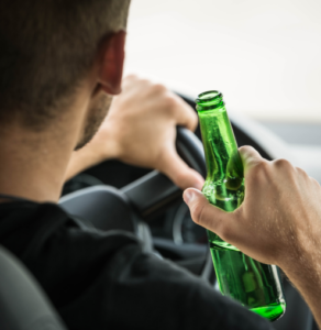 A man drinking beer behind the wheel of a car
