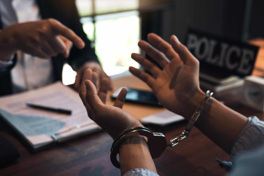 Handcuffed suspect speaking with a police officer during an interrogation, representing criminal investigation, arrest, and defense attorney services