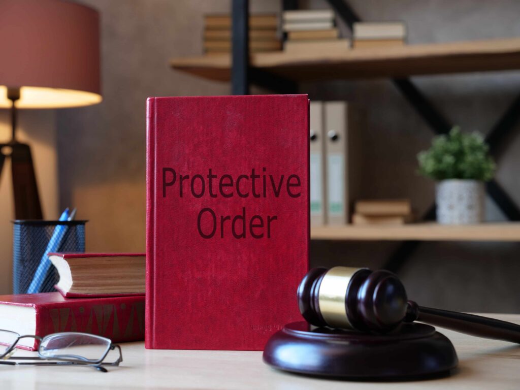 Protective order law book next to a judge&rsquo;s gavel on a desk, representing restraining orders and legal protection in court.