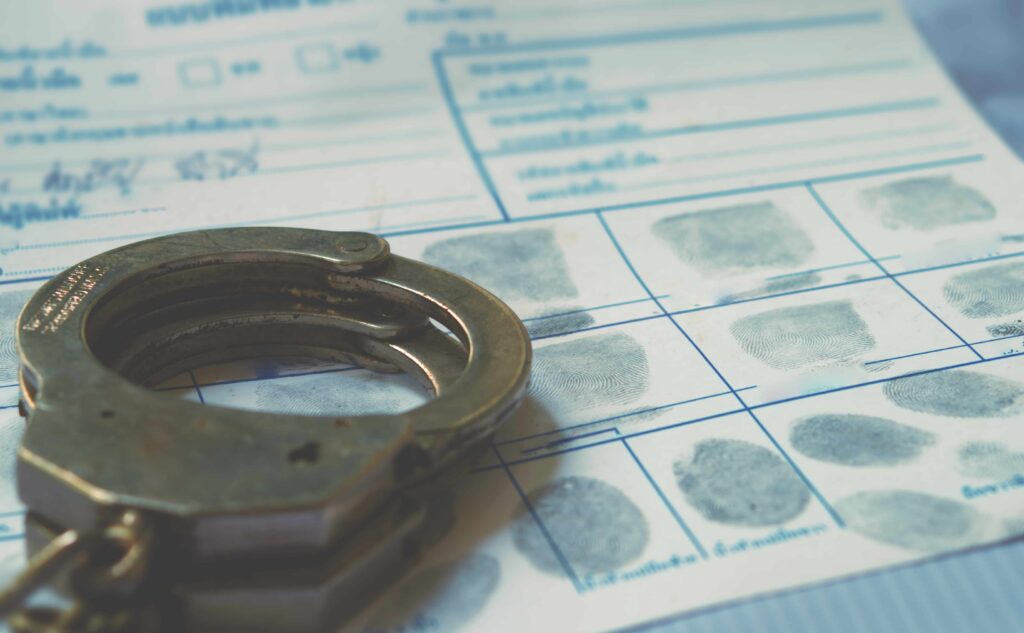 Handcuffs resting on a fingerprint record card, symbolizing criminal investigation, arrest records, and law enforcement evidence