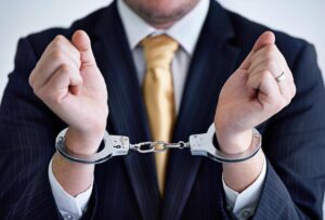 Businessman in a suit wearing handcuffs, symbolizing arrest, criminal charges, and legal defense representation.