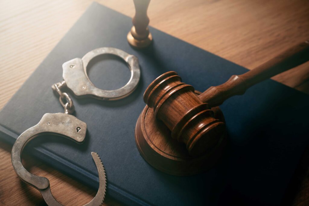 Judge&rsquo;s gavel and handcuffs on a law book, symbolizing criminal justice, arrest, and legal defense representation.