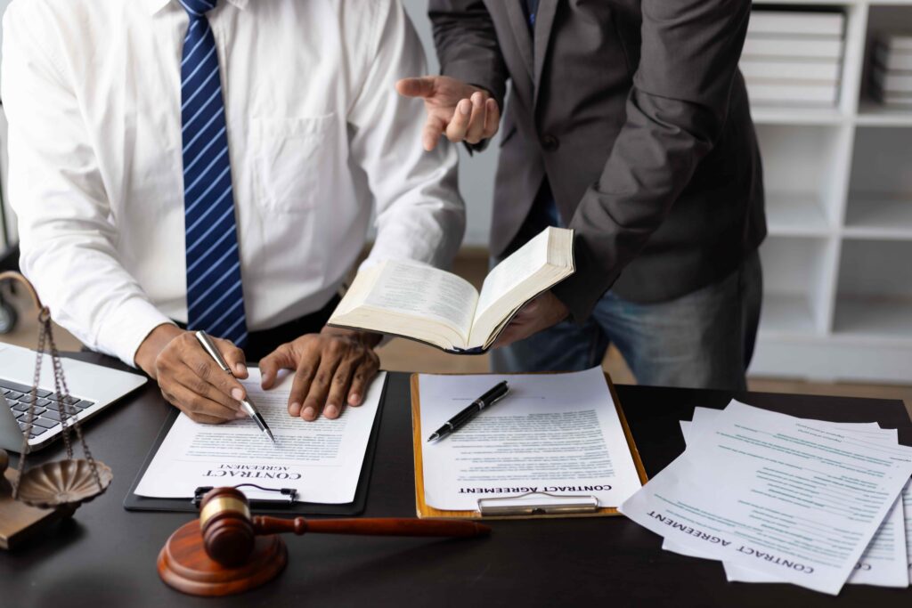 Lawyer reviewing contract documents with a client at a desk, with legal paperwork, law book, and judge&rsquo;s gavel, representing professional legal advice and agreement signing