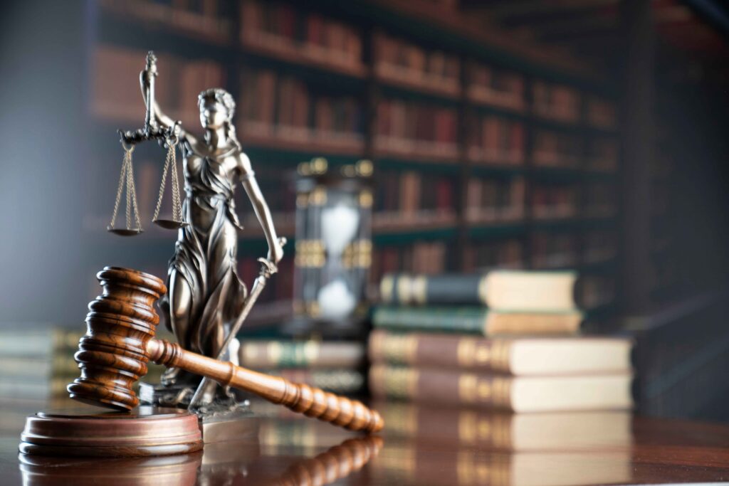 Judge&rsquo;s gavel and Lady Justice statue on a courtroom desk with law books in the background, symbolizing legal justice and attorney services.
