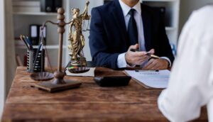 Attorney meeting with a client at a law office desk with Lady Justice statue, scales, and a legal contract, representing professional legal consultation.